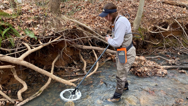 Researcher using metal detector in local stream